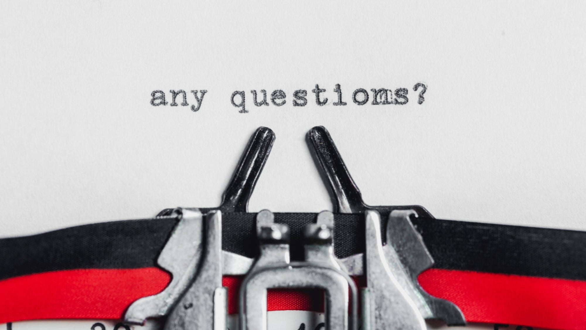Close-up of a typewriter with 'any questions?' text on a white background