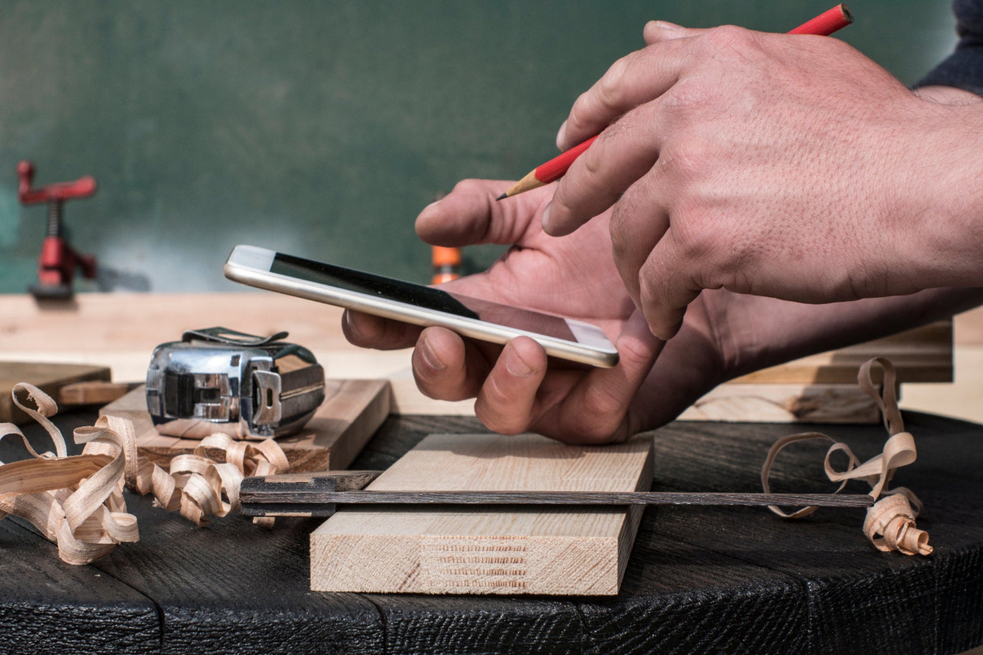 Person using a smartphone on a wooden workbench with tools in the background