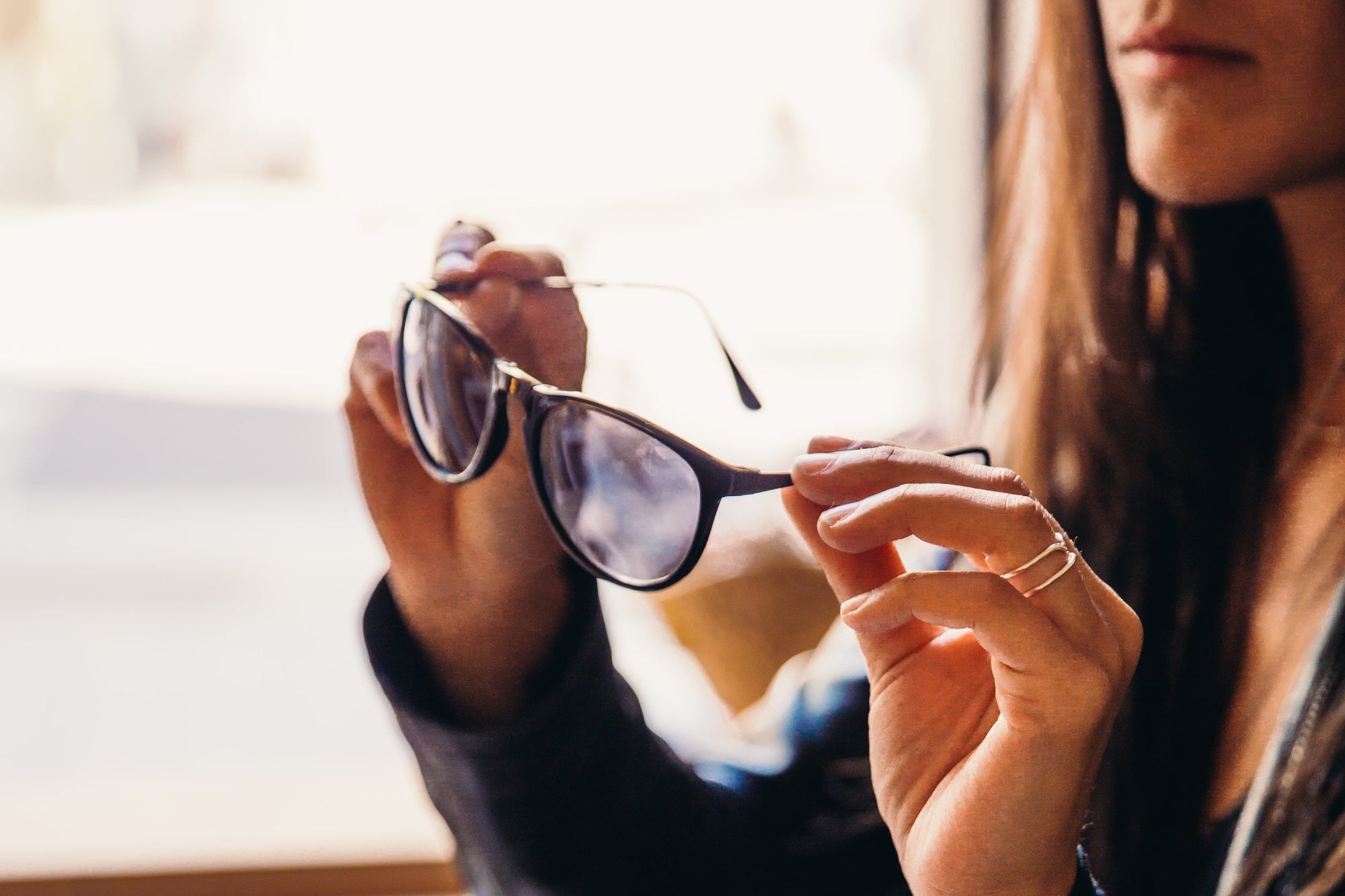 Person holding a pair of sunglasses with a blurred background